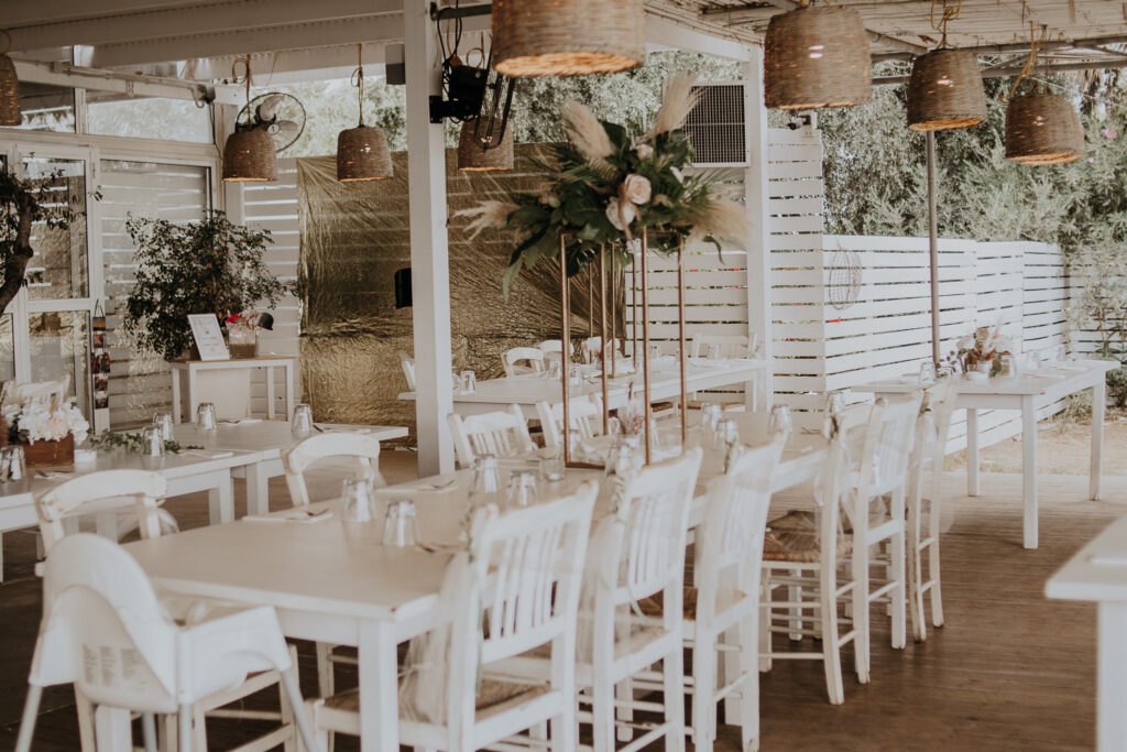 Outdoor wedding venue in Protaras featuring tall floral centerpieces on a long tables, white classic chairs and rustic details