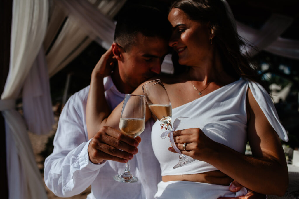 09-09-2024 (124 of 168) Bride and groom enjoying their first glass of champagne during sunset, celebrating their beach wedding in Ayia Napa, Cyprus, with the stunning sunset in the background