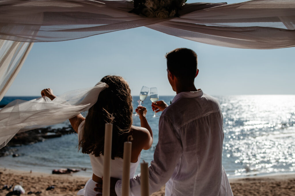 bride and groom drinking a glass of Prosecco watching the sea after their wedding ceremony at Ammos Kampouri near Ayia Napa Cyprus