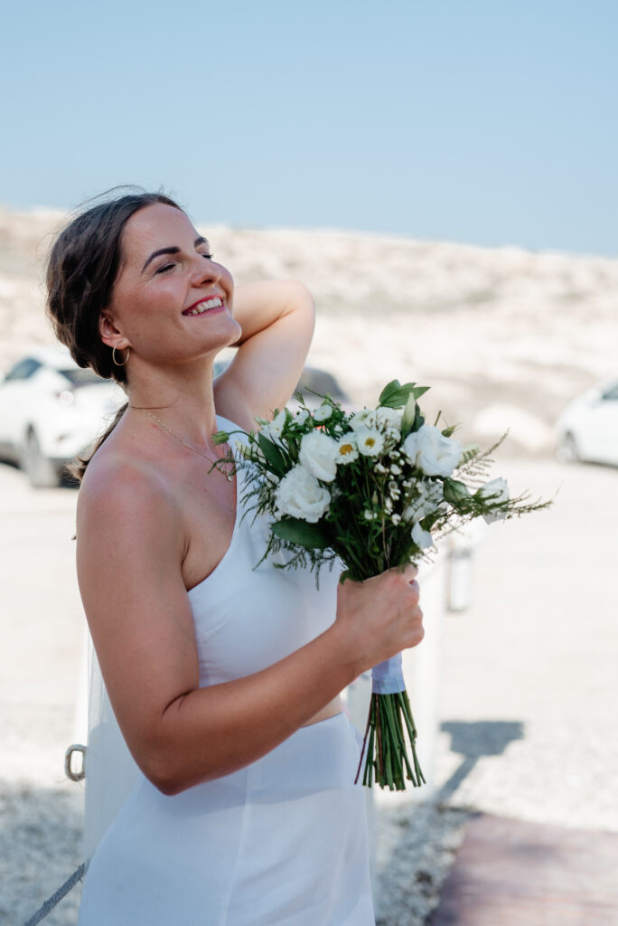 09-09-2024 (17 of 168) Smiling bride holding her fresh white and green flower bouquet just before the beach ceremony in Ayia Napa, Cyprus, radiating joy and excitement