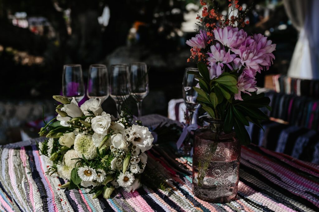 09-09-2024 (4 of 168) Elegant floral arrangement featuring white roses, daisies, and pink blossoms in glass vases on a colorful tablecloth at a beach wedding in Ammos Kampouri, Ayia Napa.