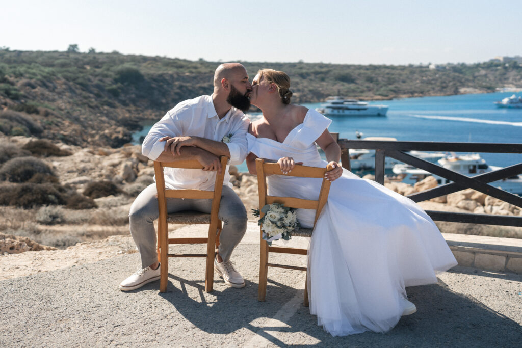 74101424_www.happyimagescyprus.com funny bride and groom photoshoot sitting on the chairs at Ayioi Anargiroi Church near Konnos Bay in Cyprus