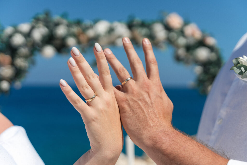 74207708_www.happyimagescyprus.com just married couple showing their hands with wedding rings in front of floral arch