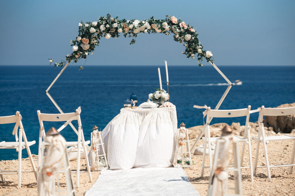 A3R03601_www.happyimagescyprus.com beautiful white geometric wedding arch with pink and white flowers, decorated ceremony table with a sea backdrop at Coralli Blue Lagoon in Cyprus