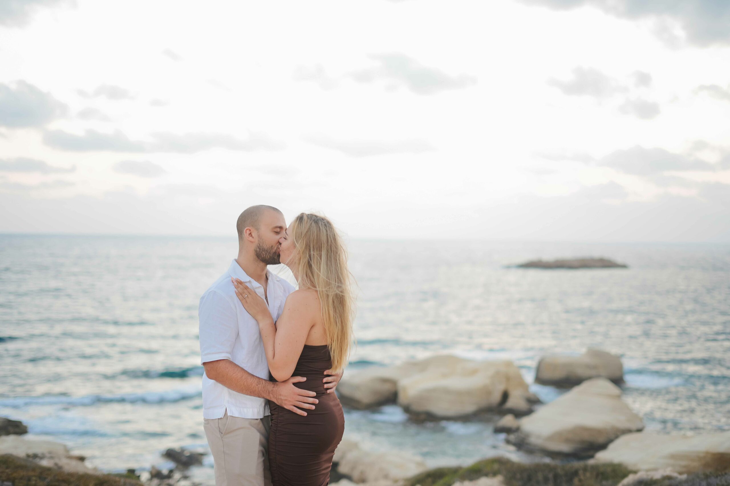 Romantic proposal photoshoot in Cyprus featuring a couple embracing by the sea at sunset, capturing a heartfelt moment against a stunning coastal backdrop.