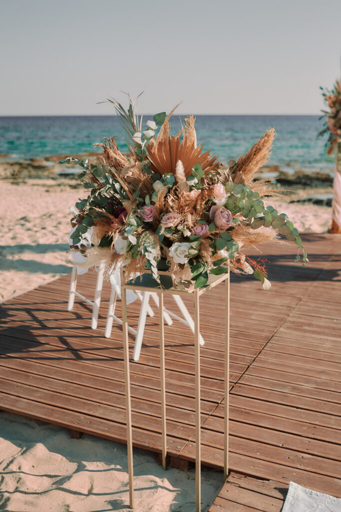 Elegant beach wedding floral arrangement featuring pampas grass, roses, and eucalyptus on a stylish gold stand at Sirens Beach, Ayia Thekla, Cyprus. Perfect for intimate ceremonies, available for wedding decoration hire and rental in Cyprus.