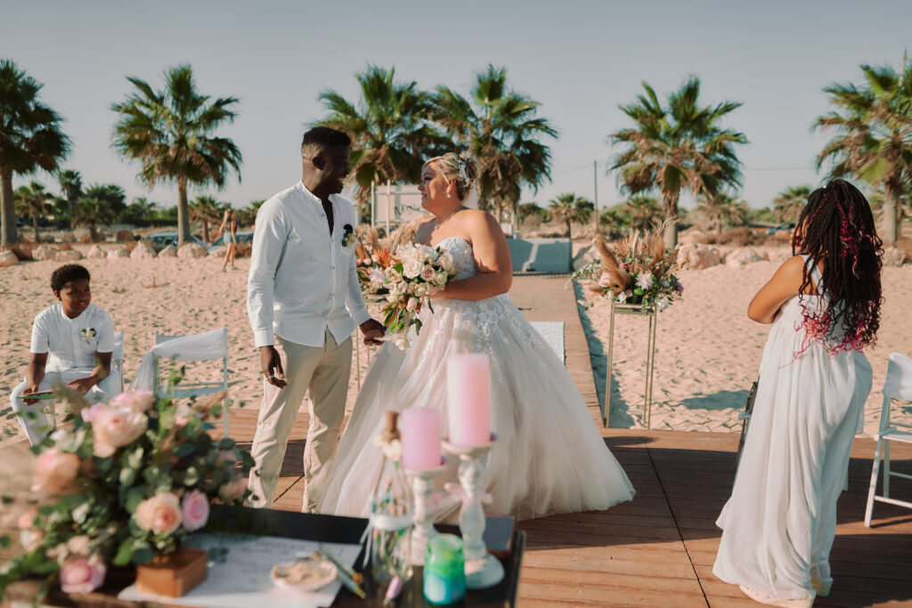 first look of the groom seeing his bride during intimate beach ceremony at Ayia Thekla beach venue in Cyprus with a palm tree and boho decorations around them