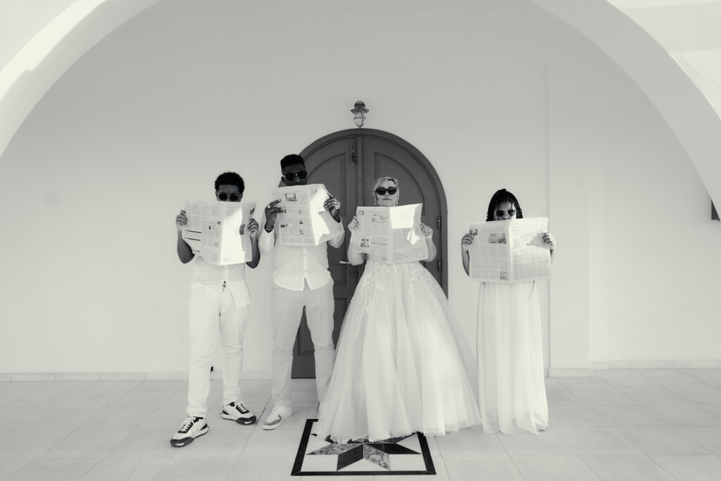 funny black and white wedding family photoshoot while bride, groom and kids are having sunglasses on and covering their faces with newspaper