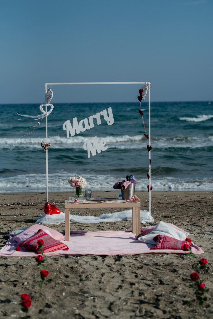 romantic beach picnic set up with a white arch and Marry me sign as a part of surprise engagement in Cyprus