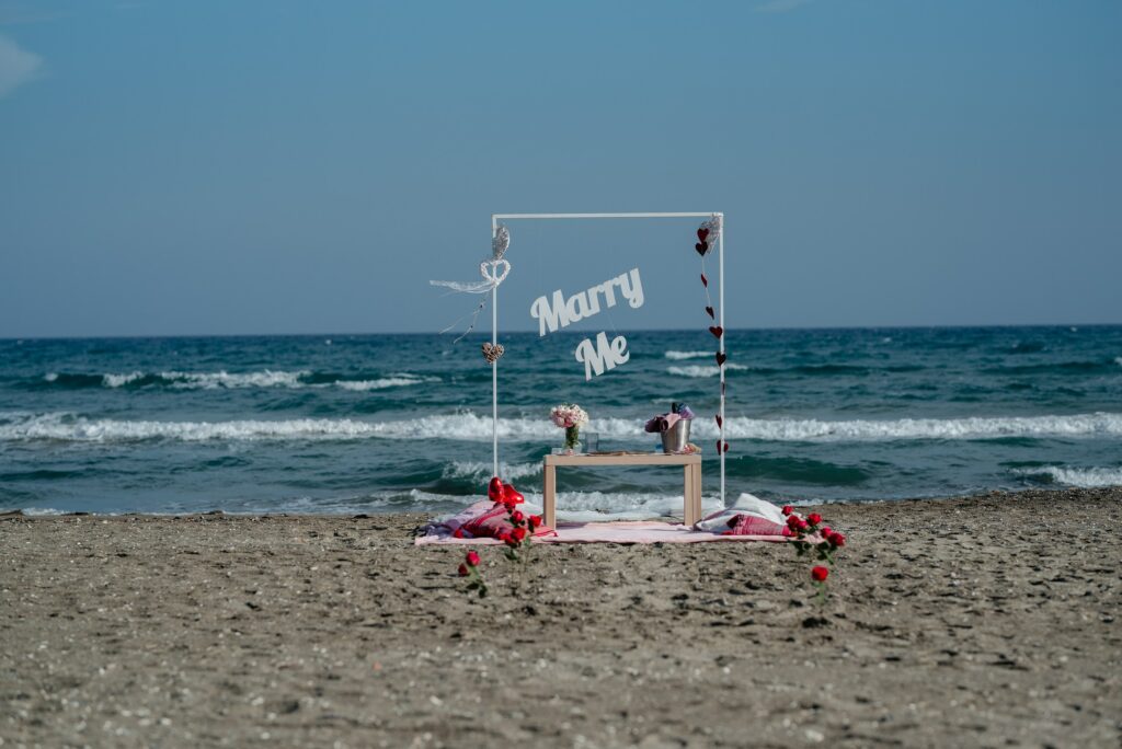 Larnaca beach wedding proposal Romantic beach marriage proposal set up with picnic table, red roses, white arch and Marry me sign