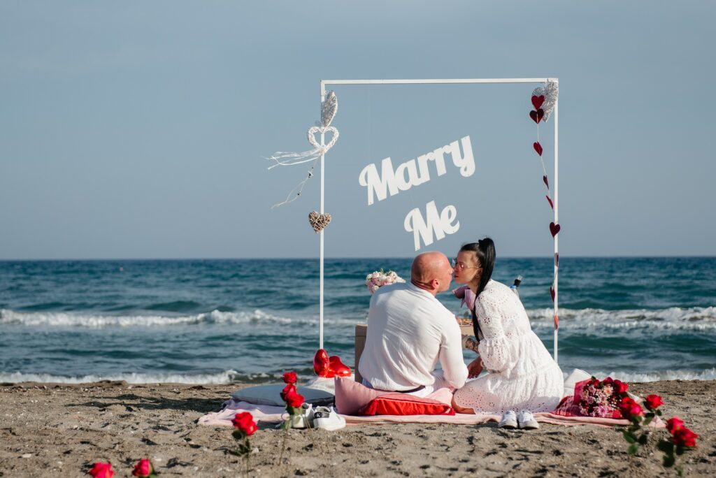 Couple kissing in front of the white arch with Marry me sign during their romantic private beach engagement in Cyprus