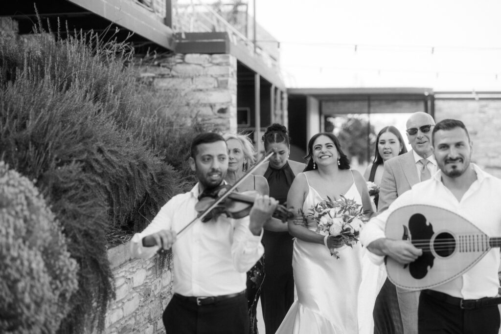 black and white photography of a bride entering the ceremony accompanied by a live Cypriot band