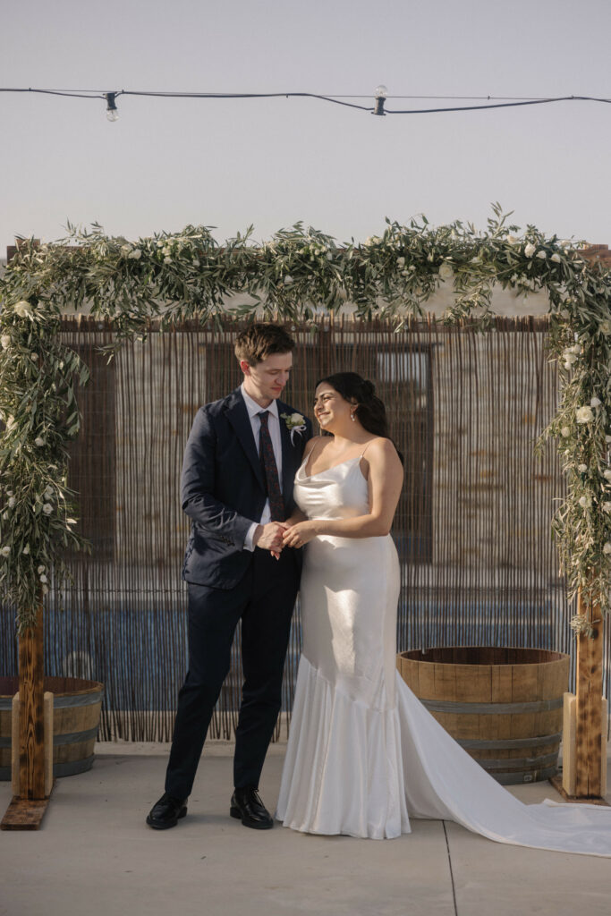 bride and groom standing in front of floral wooden arch during the ceremony in Cyprus. Wedding decoration rental services