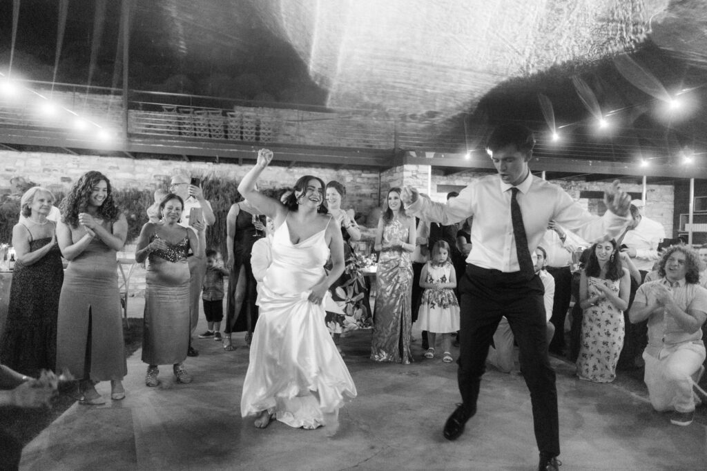 Bride and groom dancing joyfully during evening wedding reception at Dafermou Winery in Cyprus, surrounded by cheering guests under string lights and rustic stone decor from wedding decoration rental setup