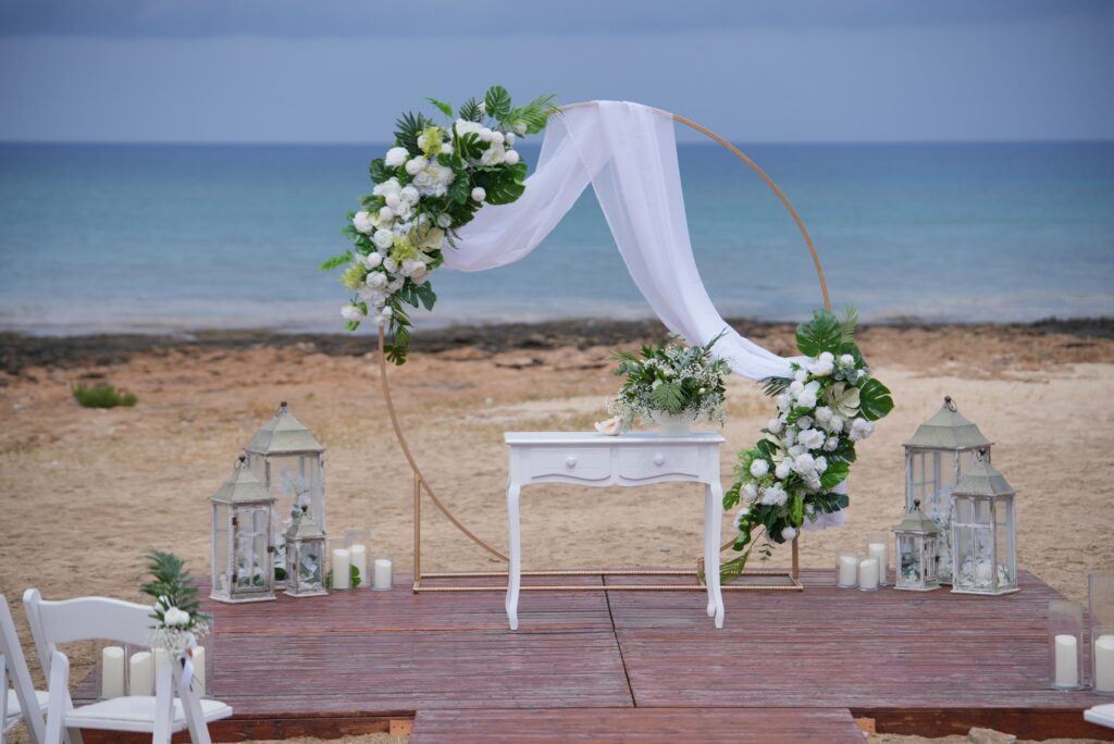 Gold round tropical wedding arch with white curtain and rustic ceremony table as a part of a wedding decoration rentals at Ayia Triada beach in Cyprus
