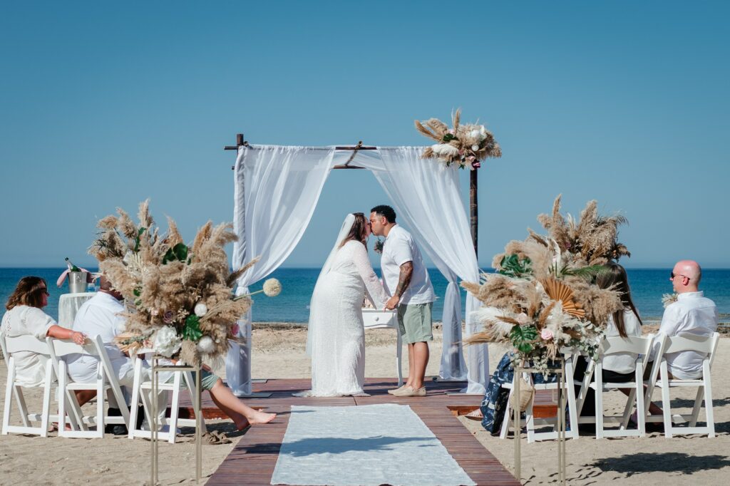 bride and groom kissing under the white gazebo with boho decorations at Ayia Triada beach in Cyprus