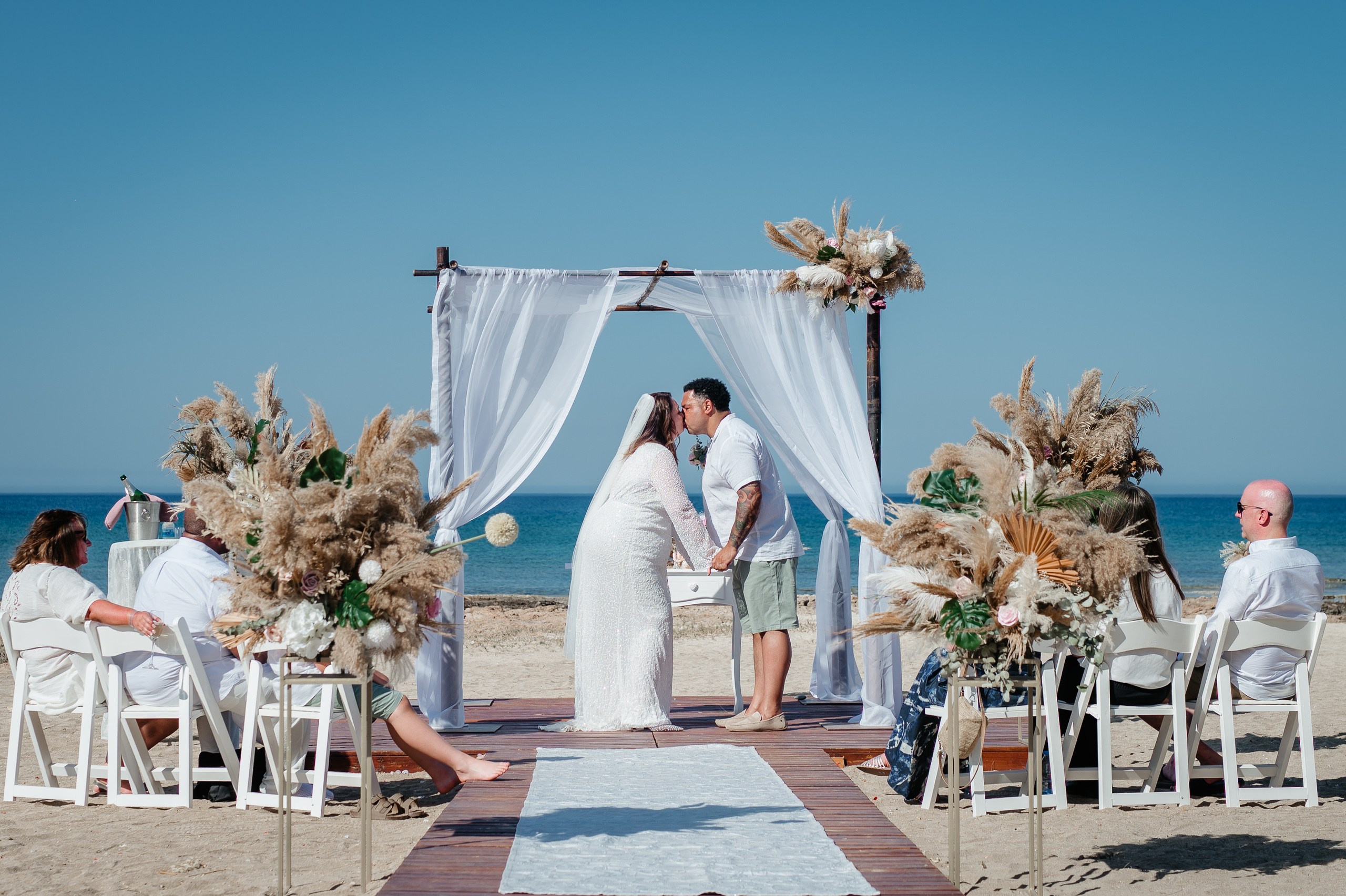 bride and groom kissing under the white gazebo with boho decorations at Ayia Triada beach in Cyprus