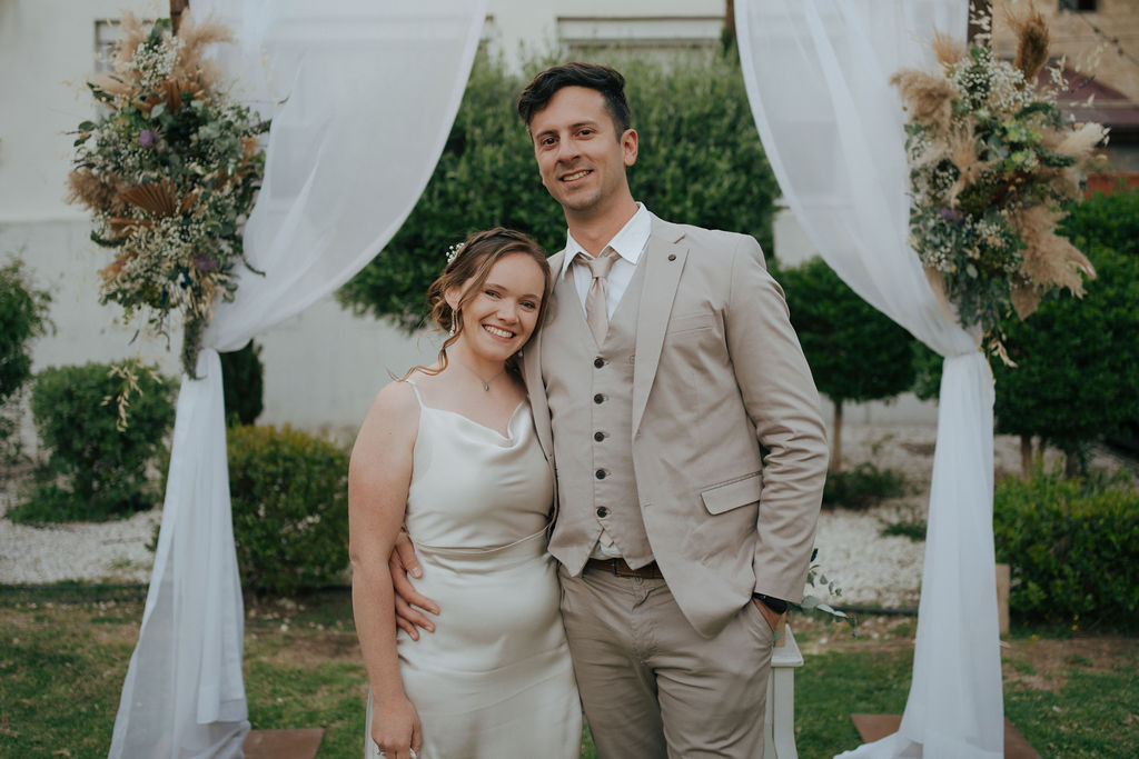 Bride and groom kissing after their town hall civil wedding ceremony in Cyprus, standing under a decorated wedding arch with white draping and floral arrangements outdoors.
