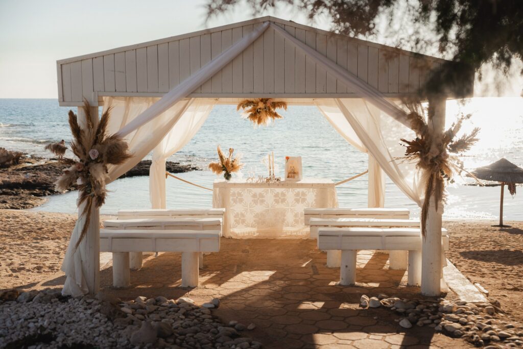 Fotografie západu slunce z bílého svatebního altánu Ammos tou Kampouri s boho dekoracemi, úžasná pro obřad na pláži v Ayia Napa na Kypru.