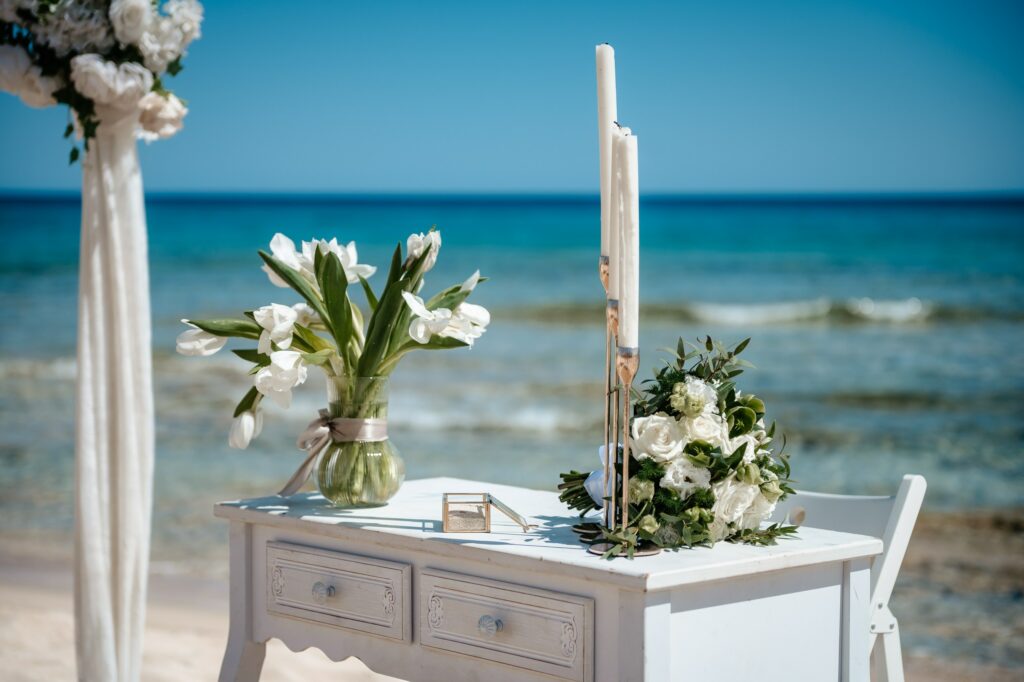 White rustic wedding ceremony table with fresh tulips and white tall candles, set against the Cyprus sea backdrop