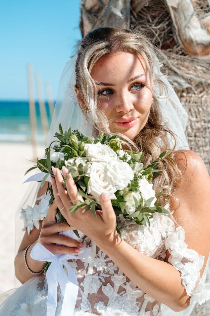 Beach portrait of bride holding fresh white roses and green wedding bouquet in Cyprus
