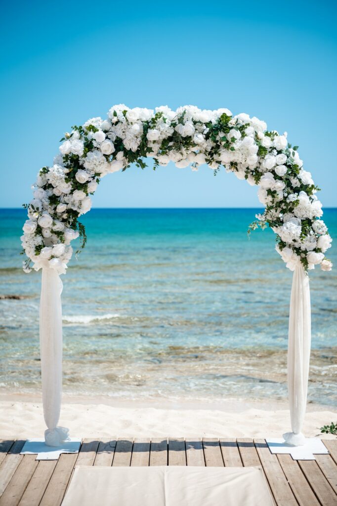 White and green floral wedding arch on wooden deck at Sirens Beach, Ayia Thekla, Cyprus