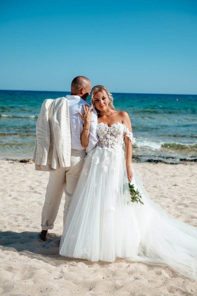 groom wearing a beige suit and bride white corset dress posing at Ayia Thekla beach wedding venue