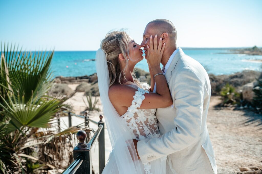 Bride wearing a white floral wedding dress and groom in a beige suit sharing a kiss at Ayia Thekla Chapel in Cyprus