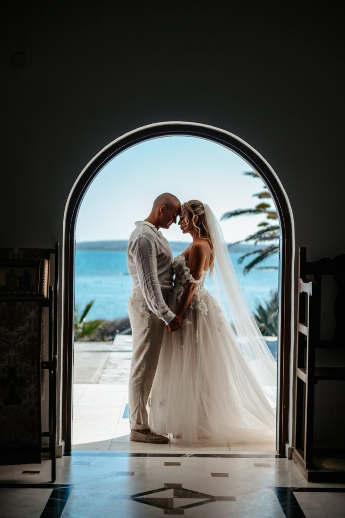 Bride and groom facing each other at the door of iconic Ayia Thekla chapel with Cyprus sea as their backdrop
