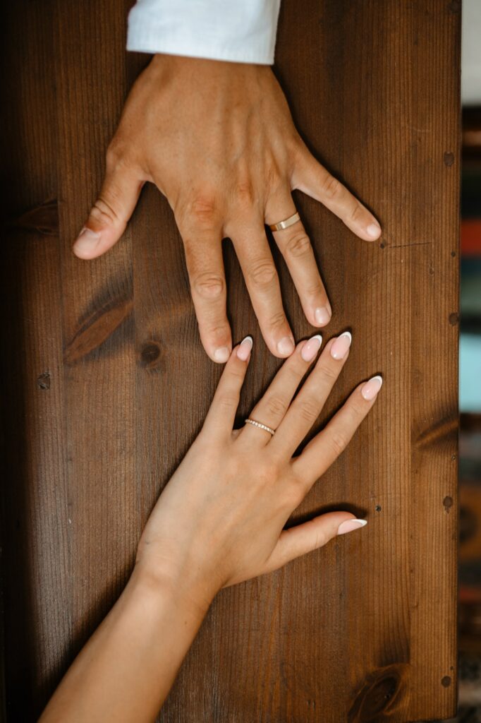 Wedding photography capturing bride’s and groom’s hands with wedding rings resting on a wooden board