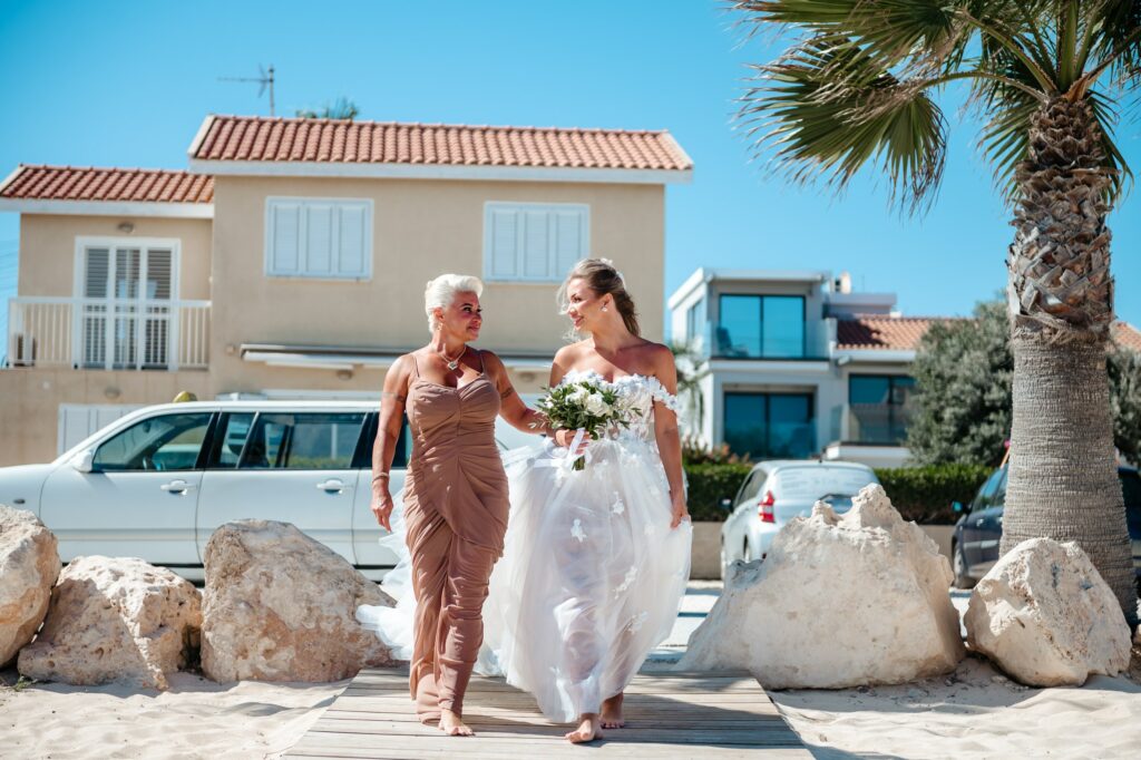 Bride and her mother walking in front of white limousine on wooden deck at Sirens Beach wedding venue in Cyprus