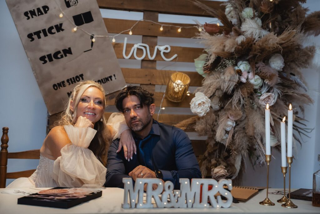 bride and groom photoshoot in front of wooden boho decorated photobooth
