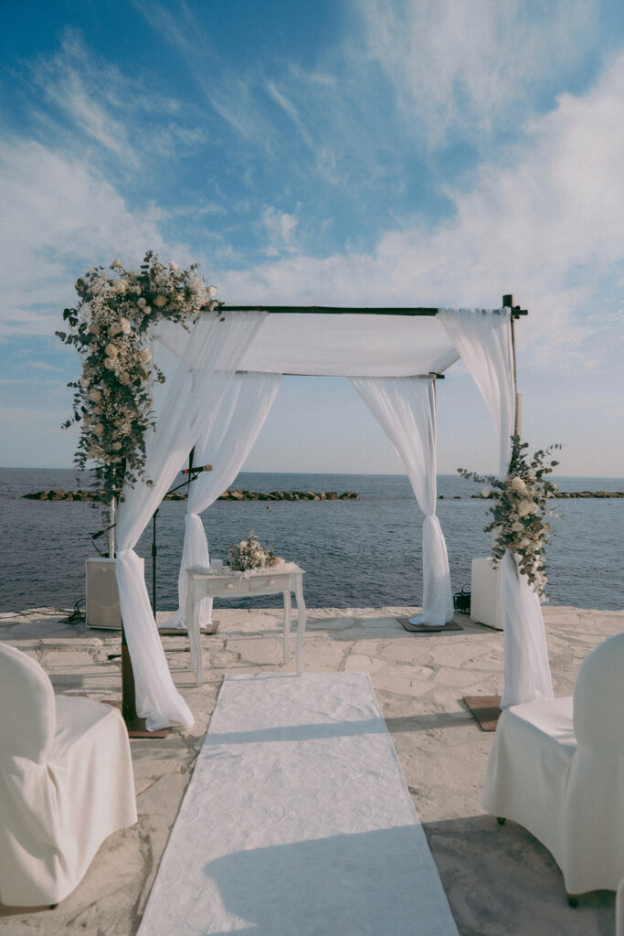 Wedding chuppah decorated with fresh white and green flowers and white drapes at Four Seasons Limassol pier