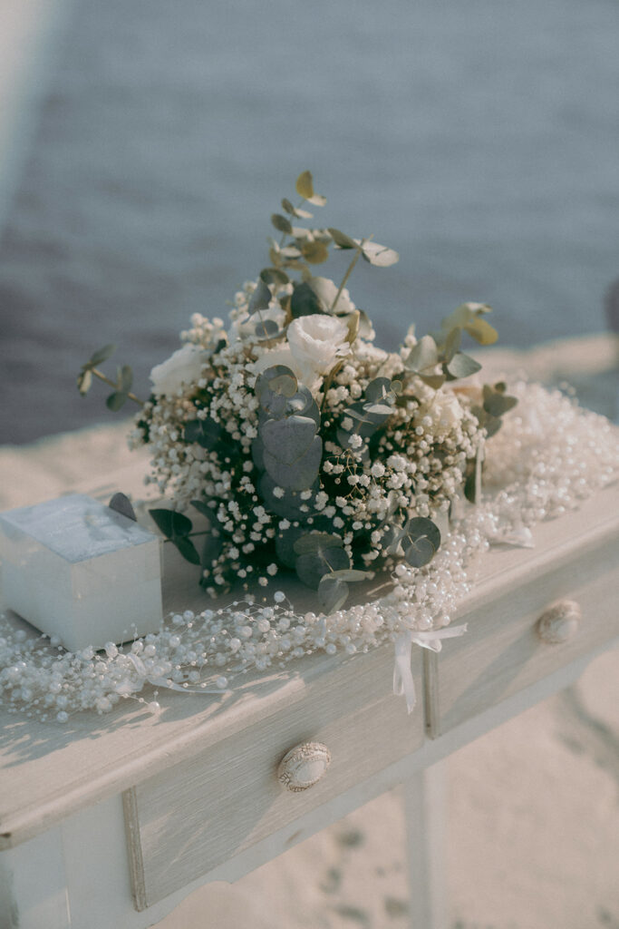 Rustic-style wedding ceremony table decorated with fresh white flowers, greenery, and white pearls