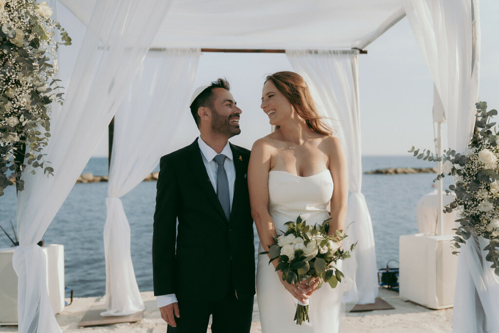 Wedding ceremony on a pier by the sea at the Four Seasons Hotel Limassol, featuring the bride and groom beneath a floral arch.