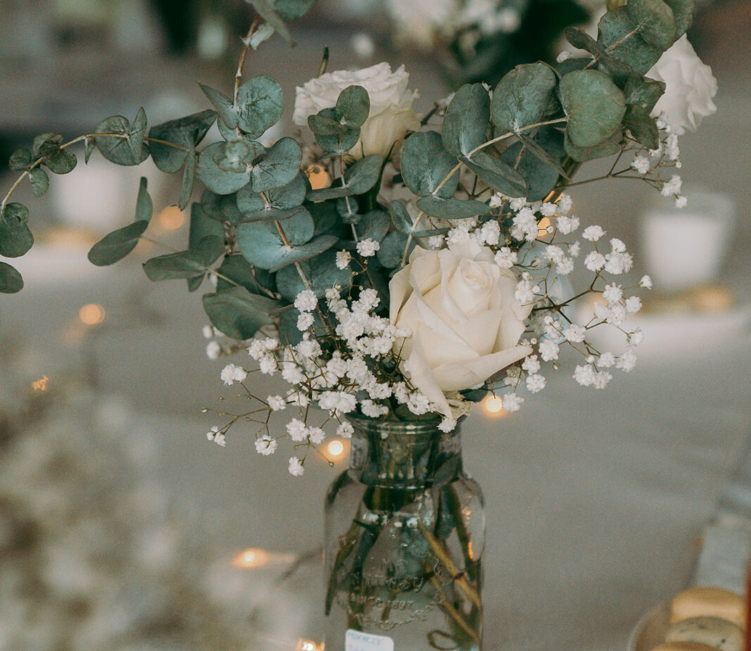 Elegant private banquet decor at Four Seasons Hotel Limassol, featuring delicate bud vase centerpieces with fresh white roses, baby's breath, and silver dollar eucalyptus. The sophisticated table setup is enhanced by romantic fairy lights, perfect for an intimate luxury wedding in Limassol.
