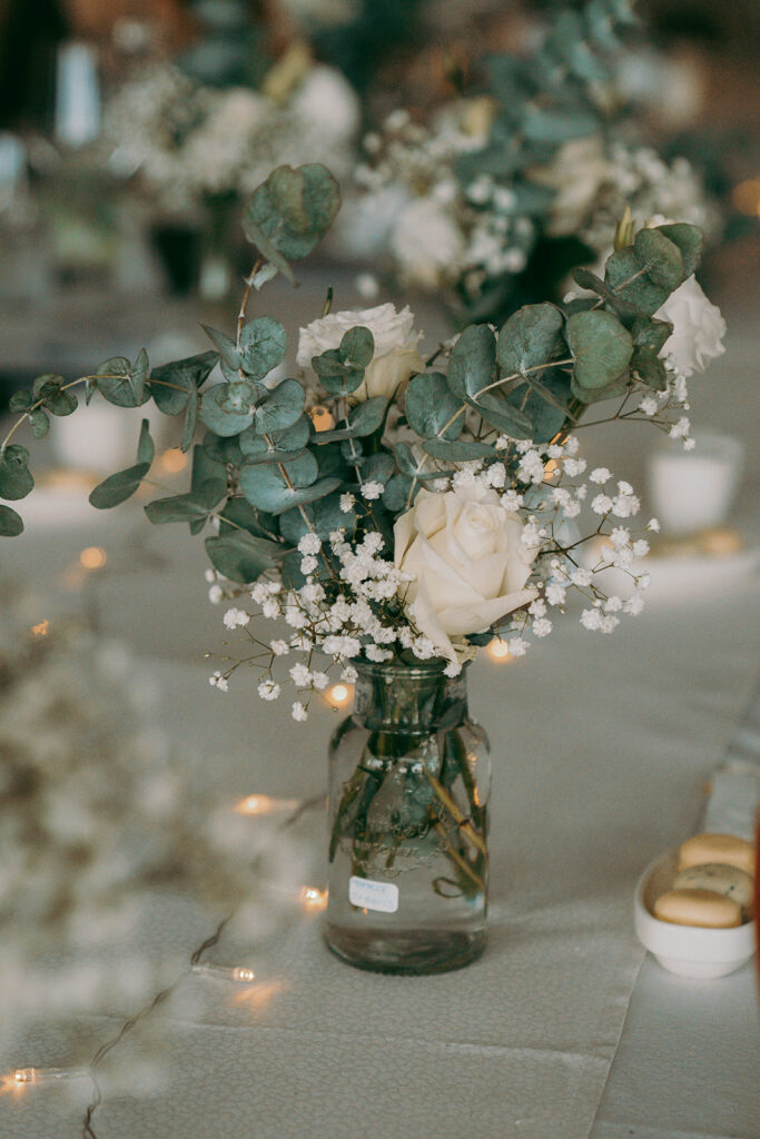 Elegant private banquet decor at Four Seasons Hotel Limassol, featuring delicate bud vase centerpieces with fresh white roses, baby's breath, and silver dollar eucalyptus. The sophisticated table setup is enhanced by romantic fairy lights, perfect for an intimate luxury wedding in Limassol.