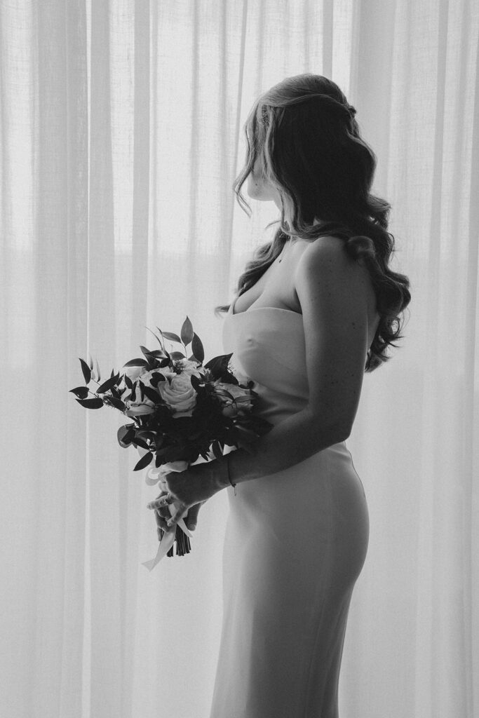 Black and white photo of bride holding a bouquet of white roses and greenery
