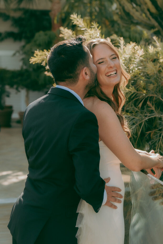 Bride smiling as groom kisses her on the cheek during romantic wedding photoshoot