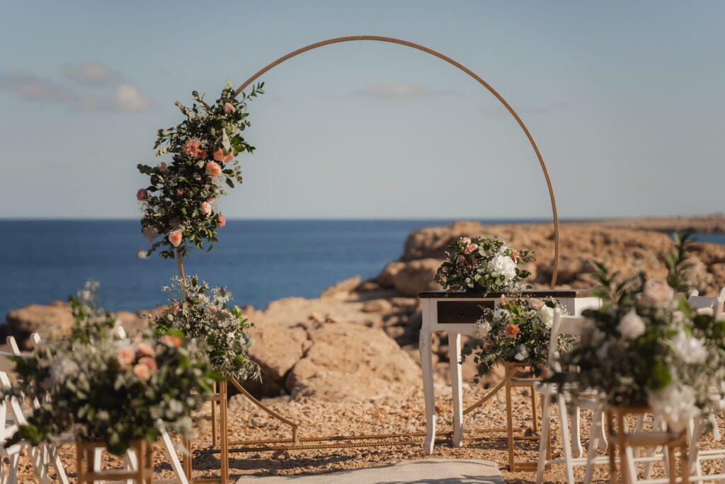 Round gold wedding arch with soft blush roses and fresh greenery and fresh floral aisle decor setup at Blue Lagoon wedding venue in Cyprus