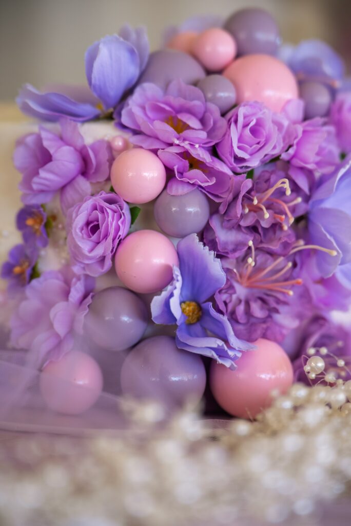 A close-up of a custom baptism cake featuring intricate purple silk flowers and pink and lilac chocolate spheres, handcrafted for boutique events in Cyprus.