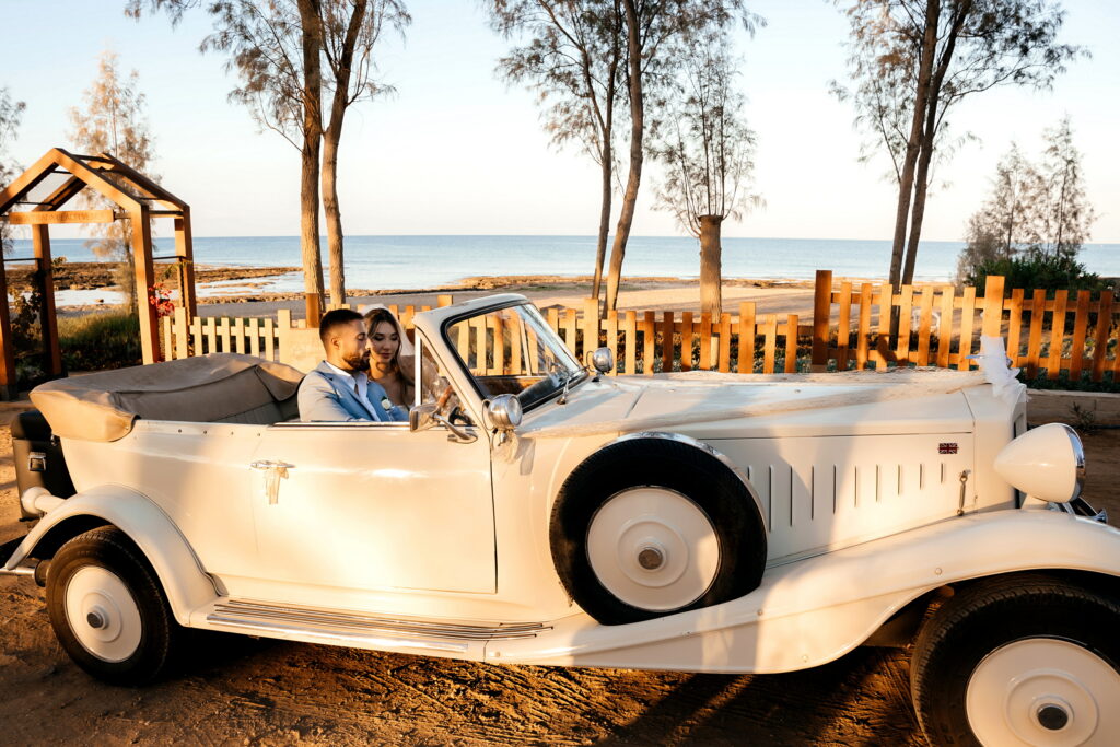 bílý vintage svatební auto s nevěsta a ženich sedí v ní na Ayia Triada pláž svatební venue