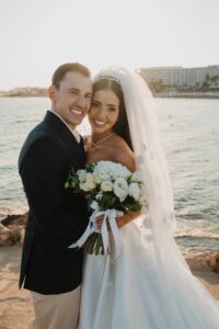 Luxury destination wedding at Nissi Beach Hotel in Cyprus, romantic bride and groom portrait by the sea with veil, bouquet, and sunset coastline