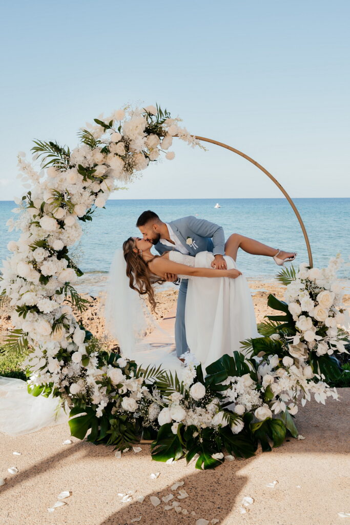 Bride and groom kissing in the middle of a luxury green and white floral circle arch at their wedding at Pernera Blue Waters venue