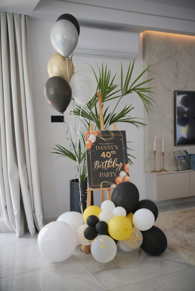 Gemini povedal Custom 40th birthday welcome sign on a wooden easel with black, gold, and white balloons. Elegant villa party decor and bespoke signage rentals in Cyprus.