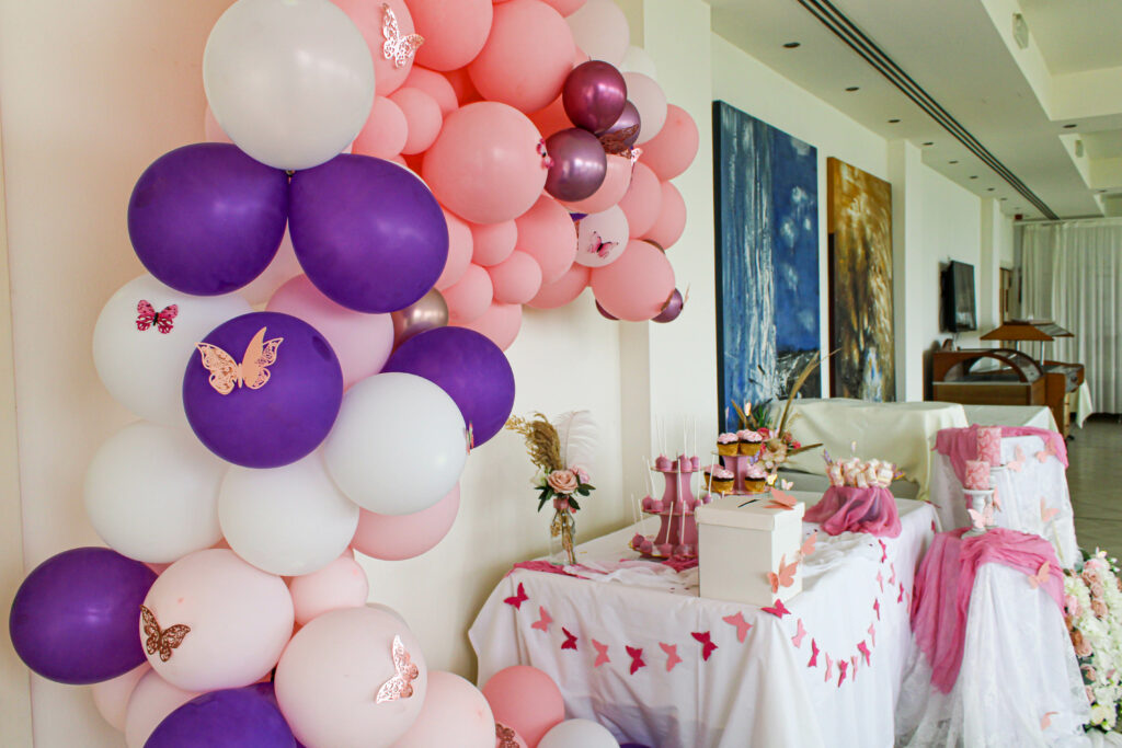 Elegant butterfly themed candy table for a girl's christening, featuring a pink, white, and purple organic balloon garland adorned with 3D rose gold butterflies. The coordinated dessert station includes custom cake pops, cupcakes, and butterfly-shaped party favors, creating a whimsical and heartfelt atmosphere for a family celebration in Cyprus.