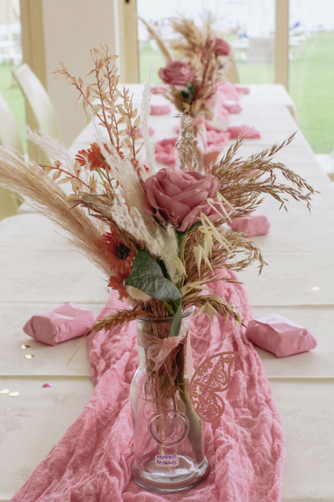 Boho-chic pink baptism party table decor in Cyprus featuring pampas grass, dried florals, dusty pink roses, and a rustic runner for a soft, elegant event style.