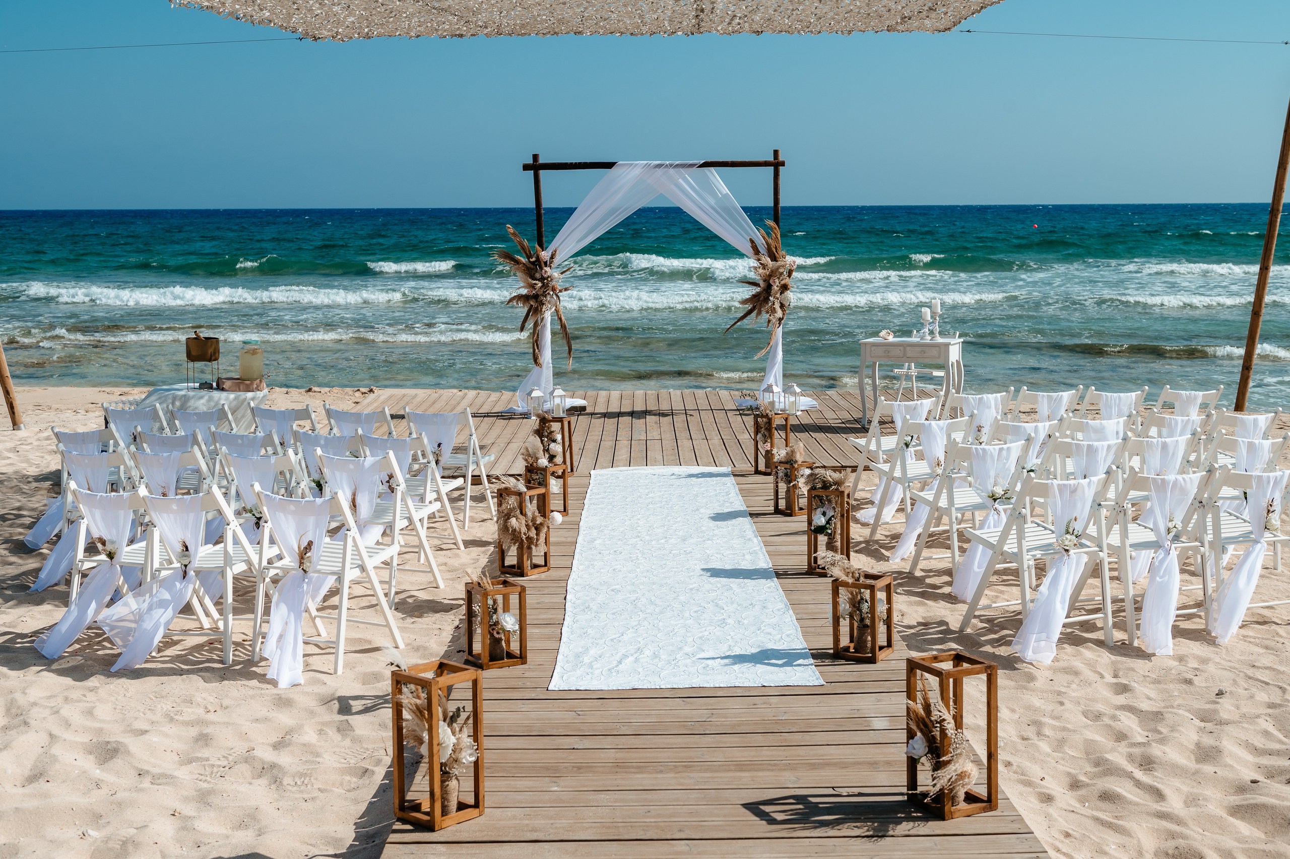 Rustic boho wedding decorations at Sirens Beach Cyprus featuring wooden arch, white chairs and rustic wooden aisle decor