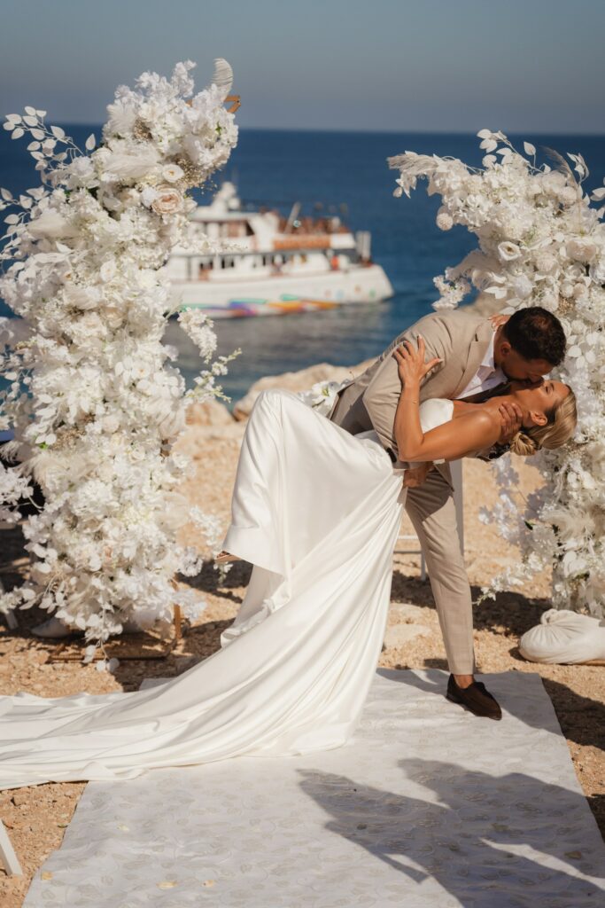 white floral wedding arch bride and groom during the wedding photoshoot in front of white floral arch at Blue Lagoon in Cyprus