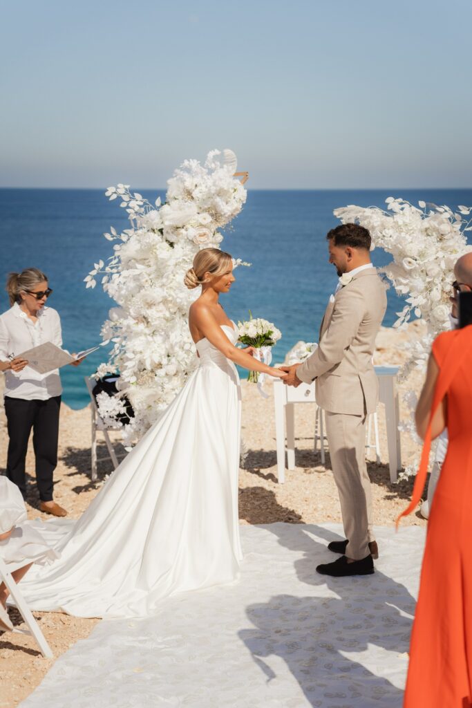 Blue Lagoon Cyprus wedding bride and groom standing in front of white half moon floral arch in Cyprus